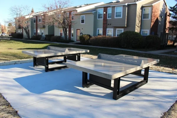Two ping pong tables in front of an apartment building.