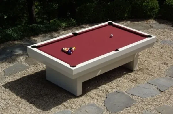 A pool table with a red cloth on a gravel patio.