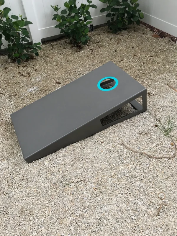A grey cornhole game with a blue circle in the middle.