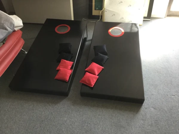Two black and red cornhole boards on the floor.