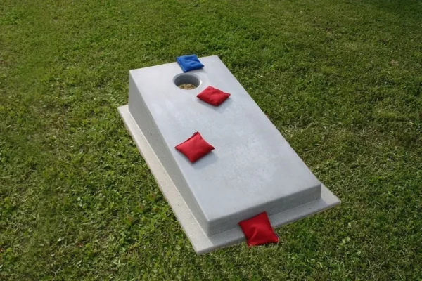 A cornhole game with red and blue pillows on the grass.