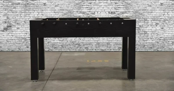 A black foosball table (Item # MO17001-FB) in front of a brick wall.