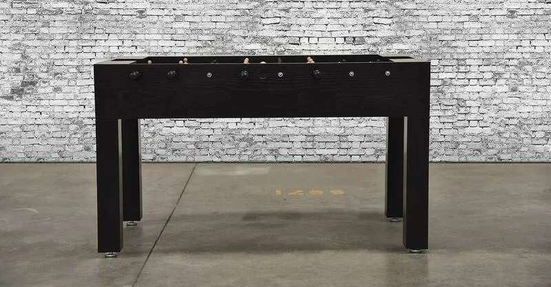 A black foosball table (Item # MO17001-FB) in front of a brick wall.