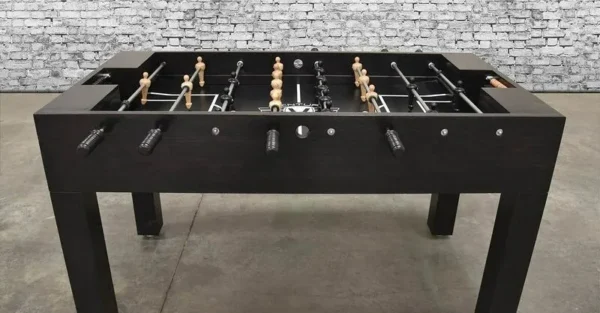 A black foosball table (Item # MO17001-FB) with wooden sticks and a brick wall.