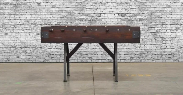 A wooden foosball table (Item # MO17001-FB) in front of a brick wall.