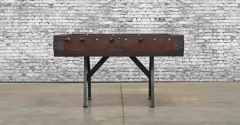 A wooden foosball table (Item # MO17001-FB) in front of a brick wall.