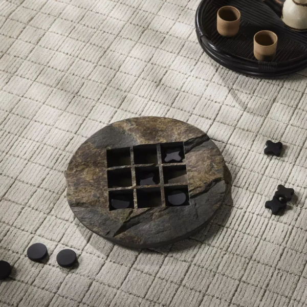A FH25032-AC tic-tac-toe game set on a woven beige carpet, with black and white pieces, some inside the board.