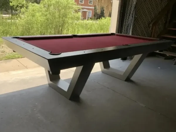 Item # GRC11047-OPT felt pool table with a unique angular base, positioned inside a dimly lit garage with a visible outdoor backdrop.