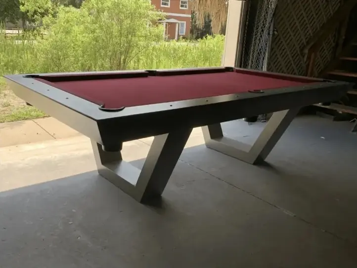Item # GRC11047-OPT felt pool table with a unique angular base, positioned inside a dimly lit garage with a visible outdoor backdrop.