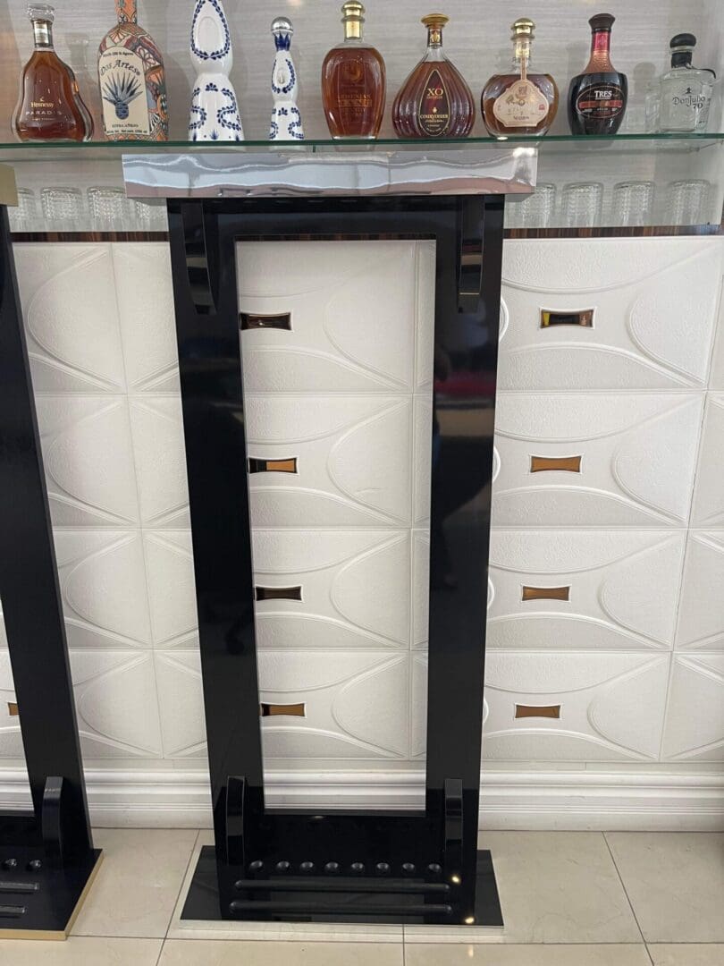 A black wooden Item # PH22029-CRW wine rack with multiple slots, standing between similar units, against a decorative tiled wall with a collection of ornate bottles displayed on top.