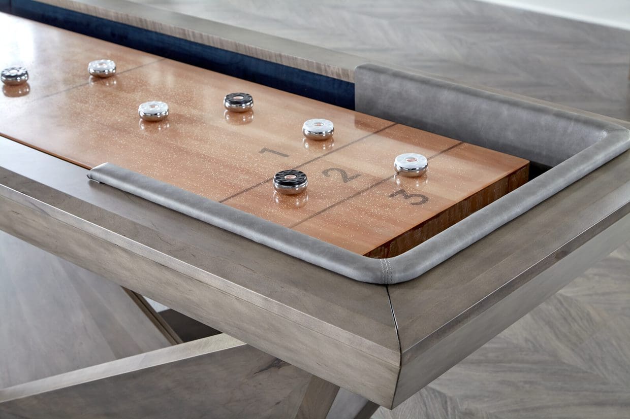 A shuffleboard table (Item # CH6045-SH) with numbered sections, showing pucks strategically placed, set against a modern home interior.