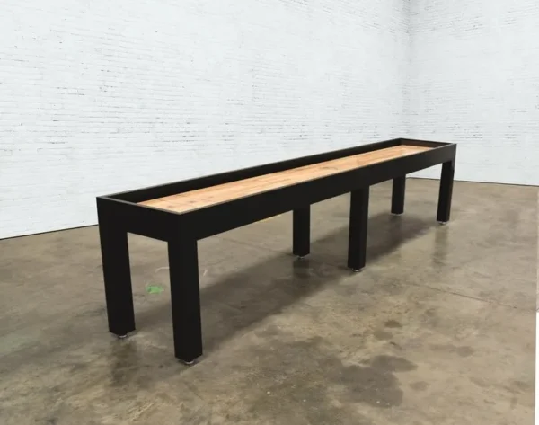 A long, narrow table with a black frame and a wooden top (Item # VG6148-SH), positioned in a room with white brick walls.
