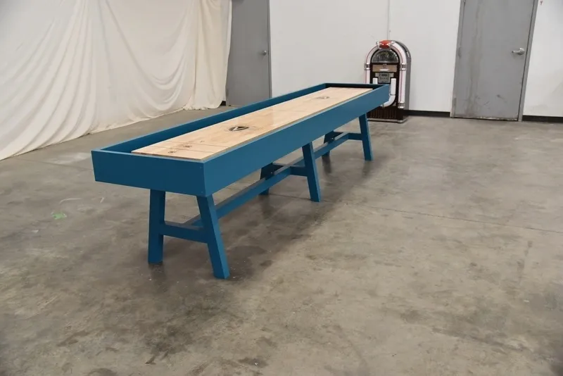 A blue Item # VG6146-SH with a wooden surface, set on a gray concrete floor against a backdrop with a curtain and a vintage jukebox.
